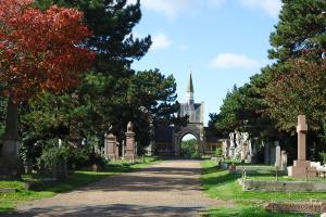 "A path leading through Hove cemetery with headstones and large trees both sides"