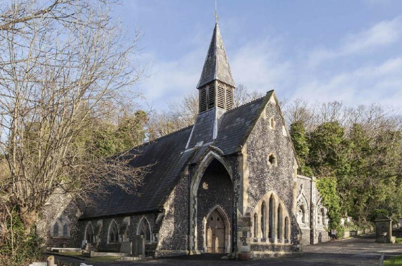 "View of the Extra-Mural chapel from outside. The chapel has a steeple and a covered arched area outside the wooden entrance doors."