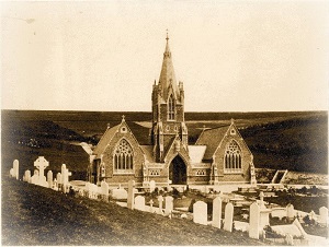 "An old sepia photograph of Woodvale burial chapel after its opening in 1857. A building with a central steeple and chapel rooms either side. There are tomb stones in the foreground."