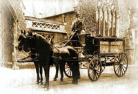 "An old sepia photograph of a horse drawn hearse arriving at Woodvale chapel"