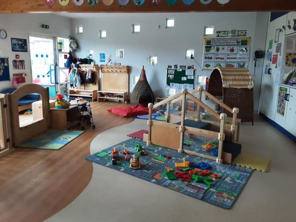 "Sunshine room at acorn nursery. Two play pen areas in front of a big window. In front of this are children's tables and chairs."