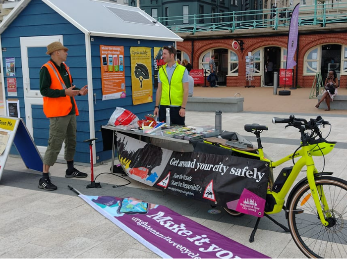 "two men in hi vis jackets standing next to a beach hut and bicycle"