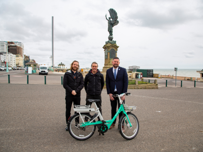 Three people standing in front of a statue with a green bicycle
