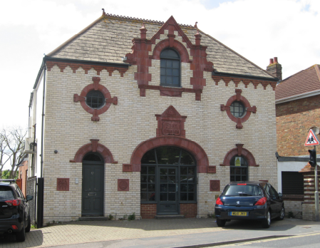 White glazed brick with terracotta dressings and hipped roof. Generally symmetrical in design: Three arched openings to the ground floor, of which the central arch is wider. Above, central window rises through eaves height to form a small gable with finials to each shoulder. Bullseye windows set to each side.