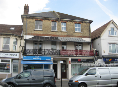 A three story house with a balcony and awning on the first floor. The top floor is exposed sandstone brickwork, the floors below are painted white.