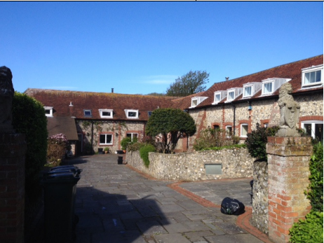 A group of buildings in an L- shape, forming a courtyard between them. They have a grey and redcrick cobblestone exterior with dark brown roofing