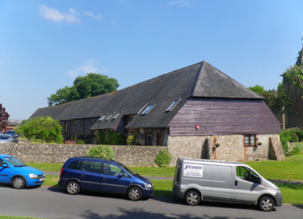 Long, low form, with flint and brick walls and a slate roof. The building is believed to be the longest surviving barn in England, 19 bays in length.