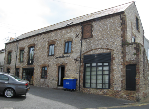 A light grey brickwork building with black framing. It is a large barn shape. On the side the words 'Crown House' are written in black metalwork