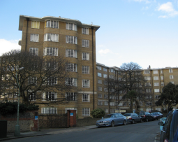 A 7 storey block of art-deco style flats. Large rectangular windows are on each floor, wrapping around the curved frontage of the brown bricked building