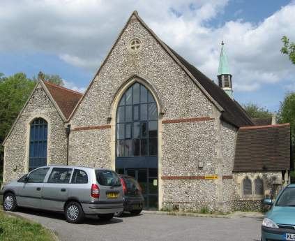 A modest grey stone church with two pointed roofs. It has been converted and large arched glass windows sit on each frontage