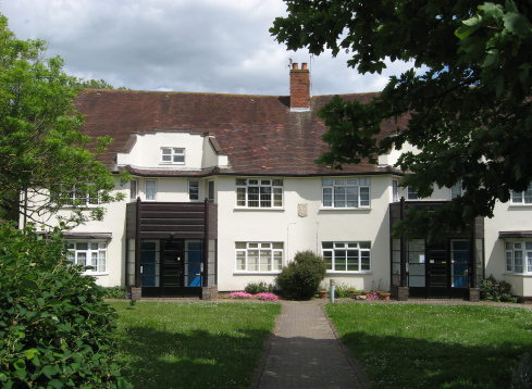 A lawn leading up to a block of flats. Mostly two storeys, some attic conversions. The building is white with brown slate roof.