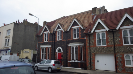 Two storey knapped flint building with red brick dressings and pitched tiled roof.  Central entrance with a canted bay window to either side. Three paired windows  above, each surmounted by a small gable with bargeboard. The doors and windows  all have Tudor gothic arches
