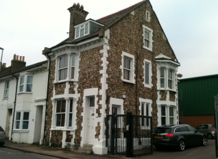 Three storey, end of terrace, victorian building with large bay windows. It is brown bricked, with ornate white edging around windows and corners