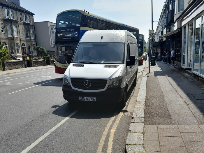 A picture of a white van parked on a double yellow line with a bus moving around it