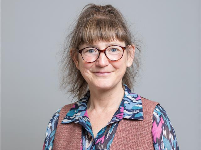 A headshot of a woman wearing glasses in front of a grey background