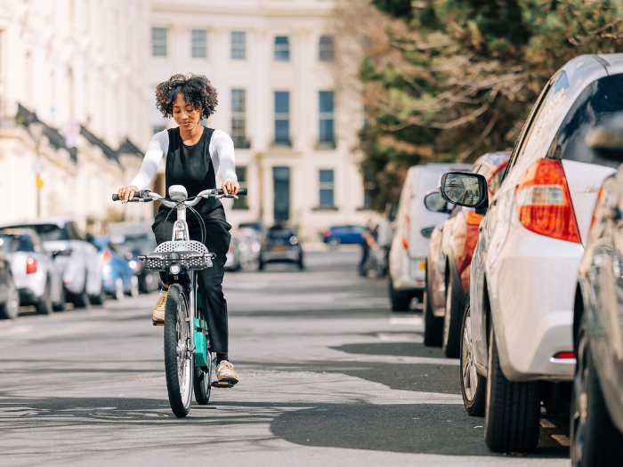 A woman on a bike, riding on a road with cars and houses either side