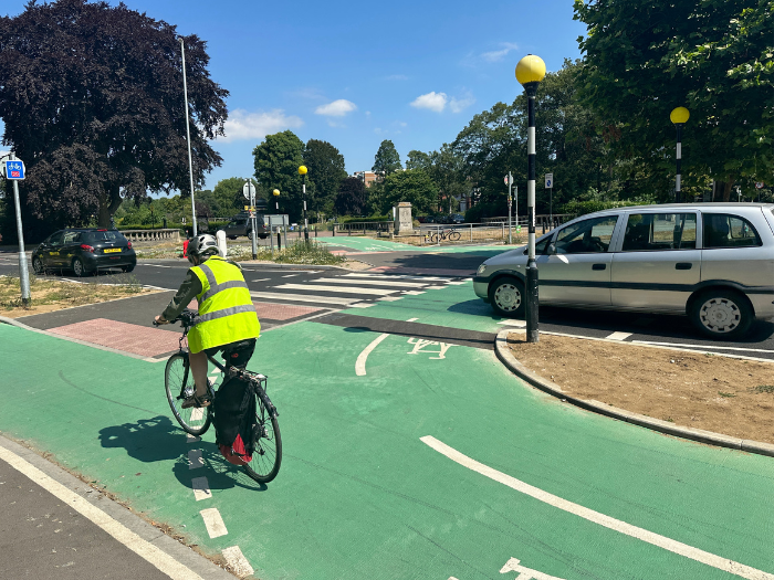 a picture of a road junction with a cyclist and a car