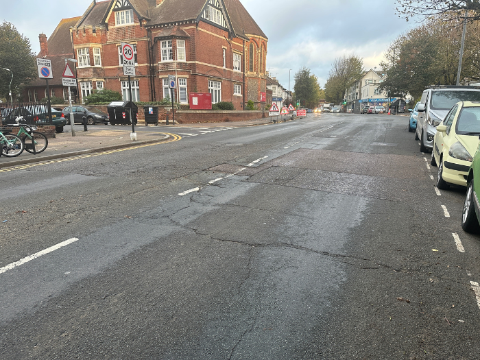 A picture of a cracked road with cars parked either side and a building in the background