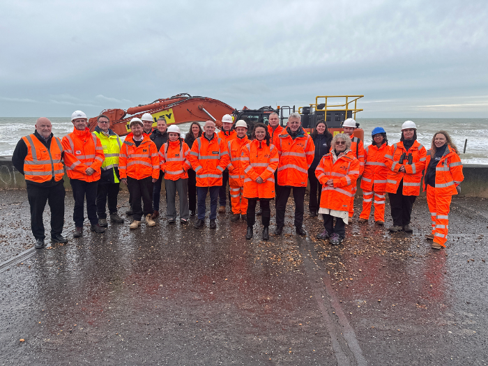 A group of people standing in front of a digger on the seafront