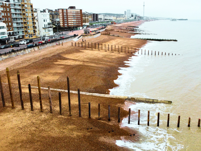 A shingle beach, the sea and buildings in the background