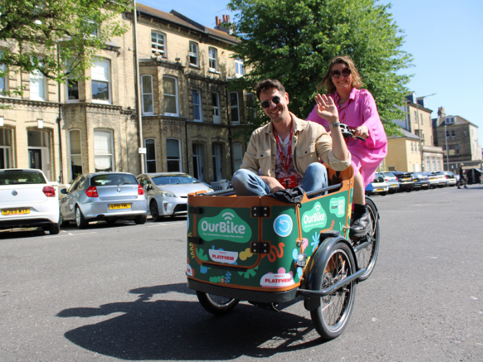 A man sitting in an ecargo bike being ridden by a woman