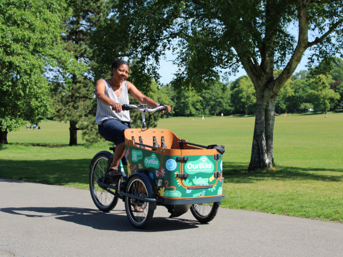 a person riding an ecargo bike on a path with a park in the background
