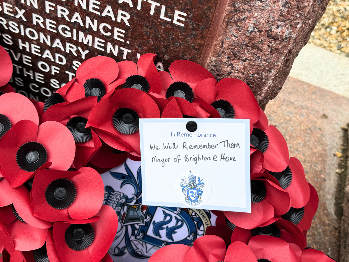 a poppy wreath with a card reading "we will remember them, Mayor of Brighton and Hove" laid against a memorial stone