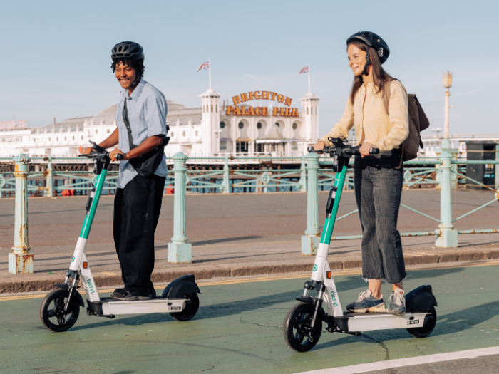 two people on e-scooters in front of a pier