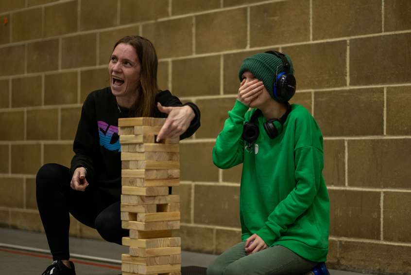 An adult and a child are crouched playing a game of big Jenga. They look surprised and happy.