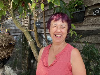 Barbara Sheppard standing in front of wooden wall and tree.