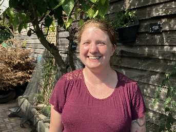 Frances standing in front of a wooden wall and tree.