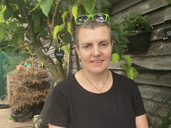 Julie standing in front of a wooden wall and tree