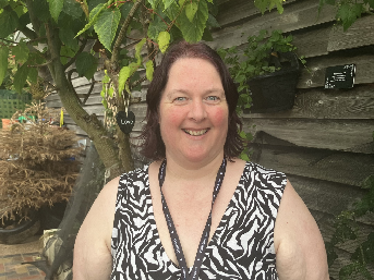 Kirsty standing in front of a wooden wall and tree