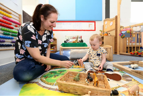 Nursery worker sitting with a baby playing with toys.
