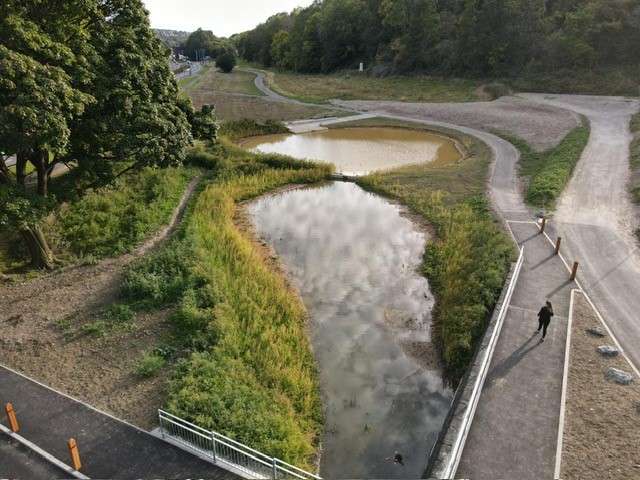 Rainscape from above. Two ponds of water next to each other surrounded by grass. A path runs along the side with a person walking along it.