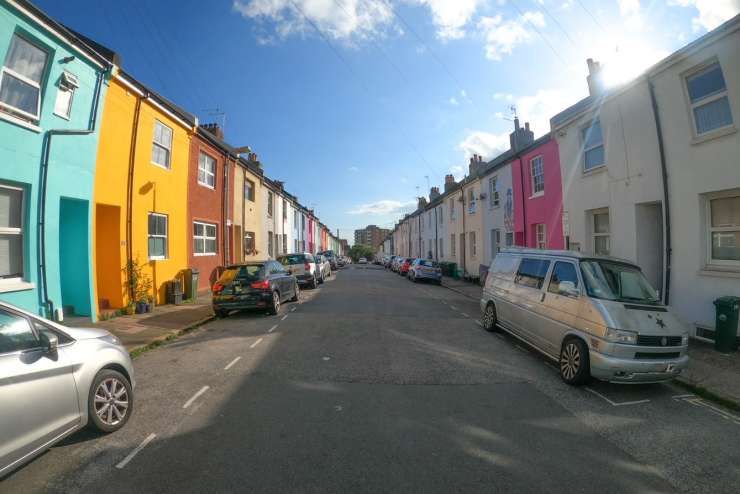A road with cars parked on each side with colourfully painted houses