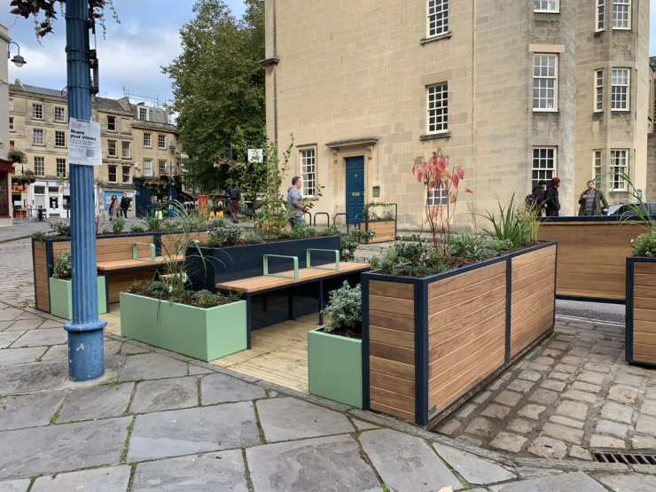 A road with wooden benches, decking and plants and a building in the background 