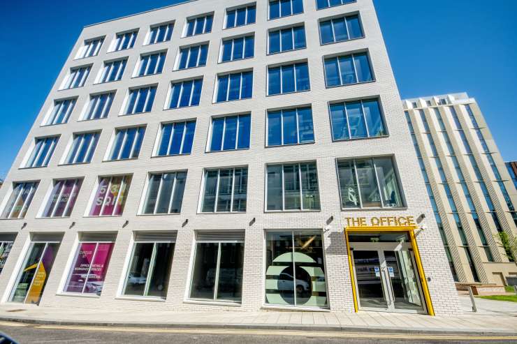 An image of the new office space, a large, white brick building with many big glass windows.