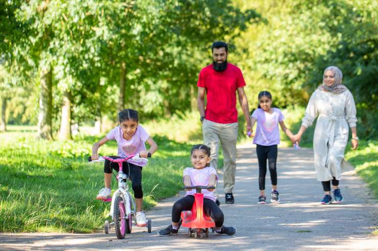 A family in a park. The parents are walking with one child, and two other children are cycling in front of them.