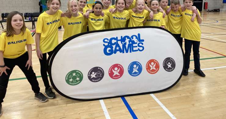 A group of school children pose for a team photo behind a banner reading 'school games'