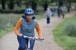 Woman cycling on a path through a grassy area.