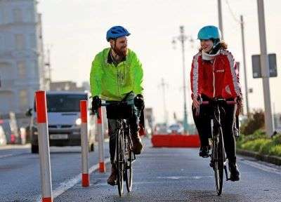 A man and a woman cycling towards the camera, along the cycle lane on Brighton seafront.