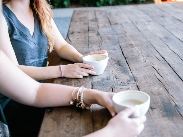 Two people having a cup of tea together at a table outside. You cannot see their faces.
