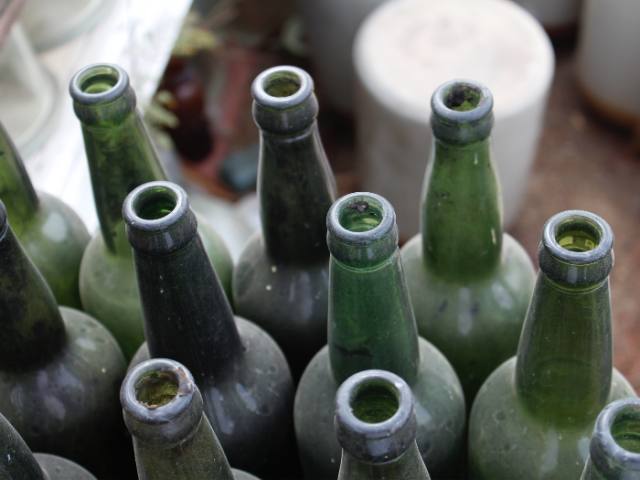 Empty green glass bottles stored near a bin. Photo by Bhavyesh Acharya on Unsplash.