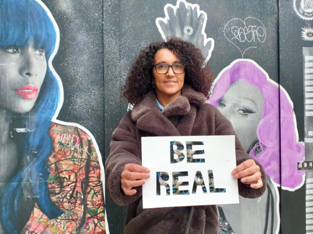 Photo of Brighton & Hove life coach Sam Adams holding a notice reading 'Be real'
