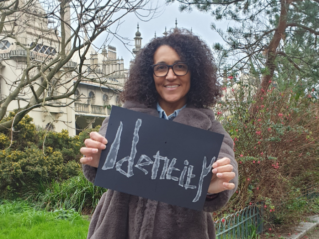 Photo of Sam Adams holding up a notice with 'Identity' written on it, the them of one of the short films she's made for LGBT+ History Month