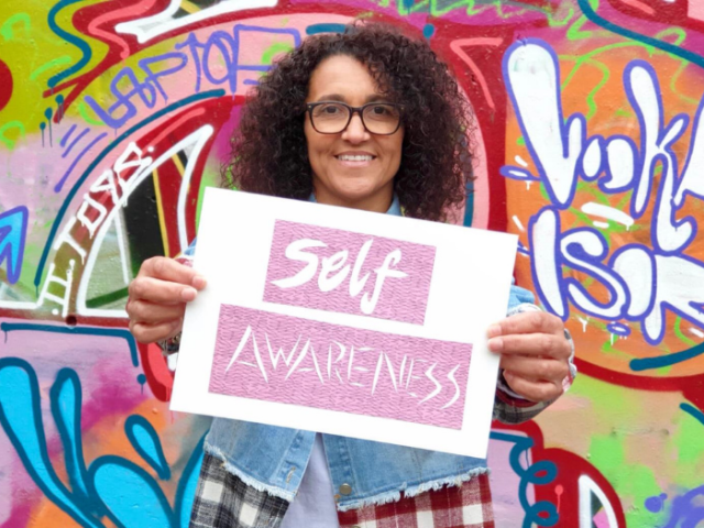 Photo of Brighton & Hove life coach Sam Adams holding a notice reading 'Self-awareness'.