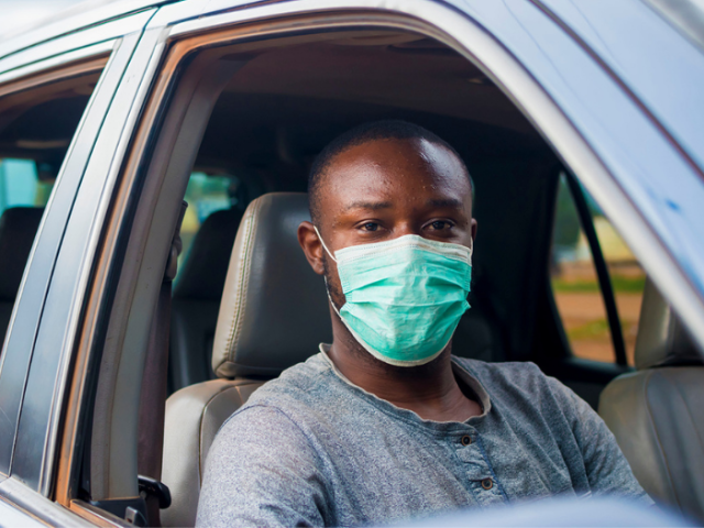 Young black man in a car wearing a grey tshirt and a disposable face mask