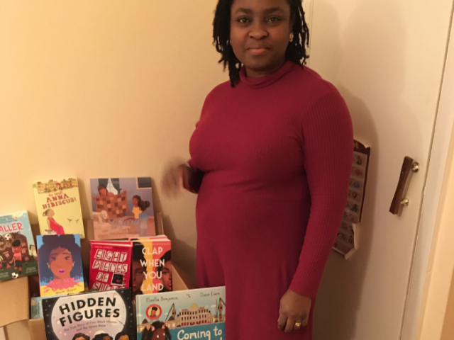 Grace Toby the coordinator of the Open Minds Project standing next to a collection of school books which feature positive black characters