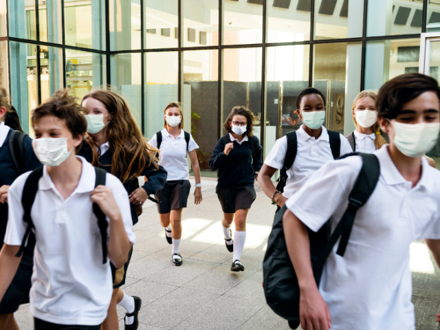 Group of school age children walking in front of school building with a masks on 